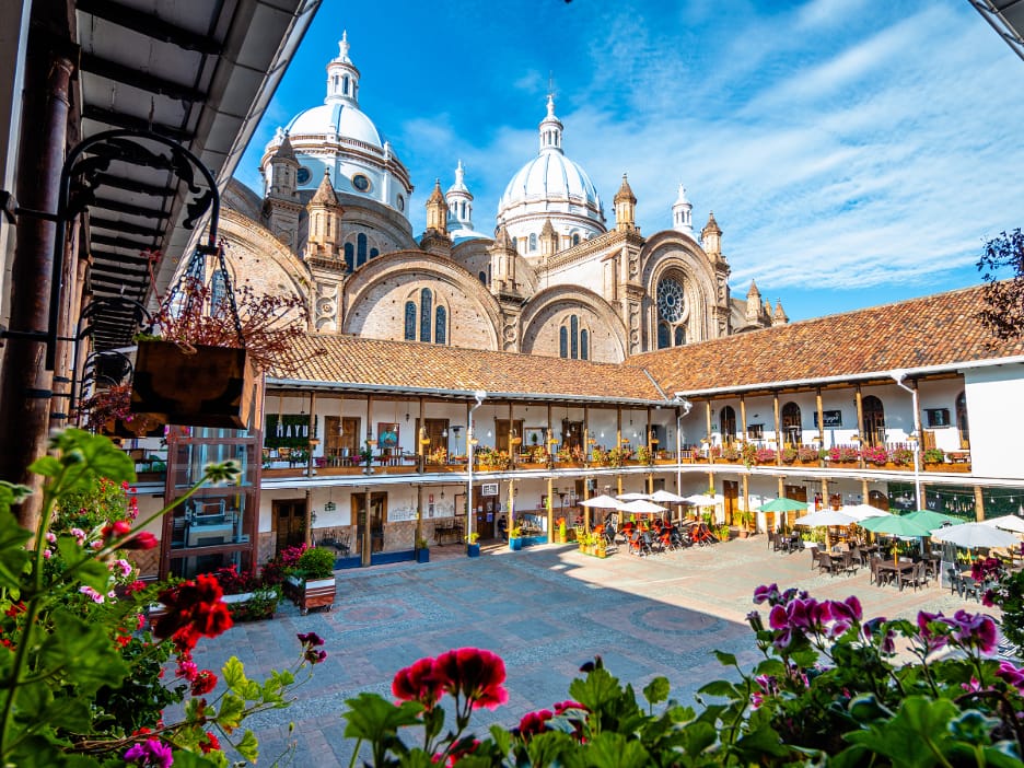 Sunlit courtyard with café tables and flowers below the white domes of the New Cathedral of Cuenca