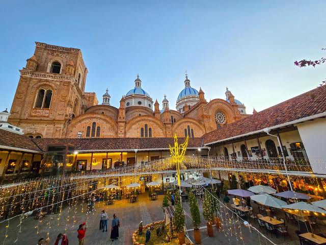 Courtyard with string lights and café tables in front of the blue-domed New Cathedral of Cuenca at dusk