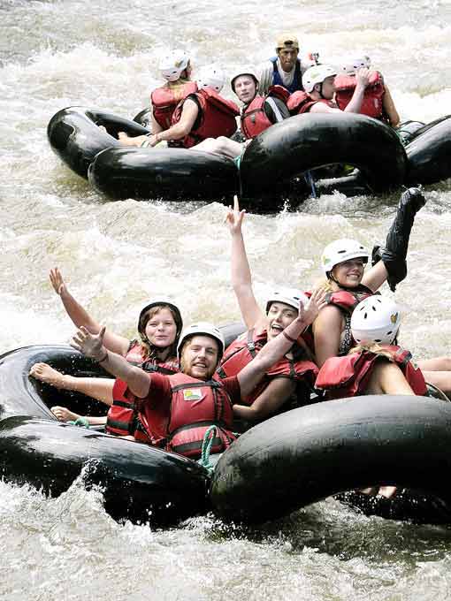 Group of smiling people in helmets and life jackets riding inner tubes on river rapids