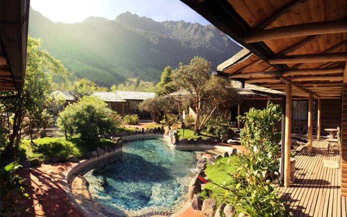 Rock-lined hot spring pool beside wooden cabins and a deck with mountain views at Termas de Papallacta